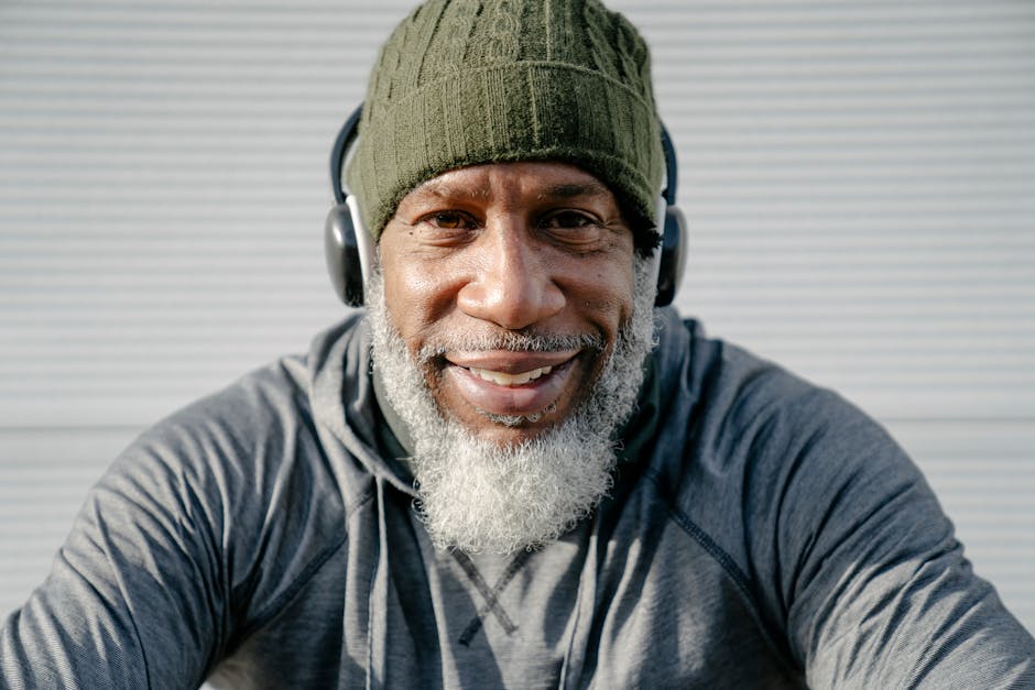 Elderly man with headphones smiling joyfully in an outdoor setting.