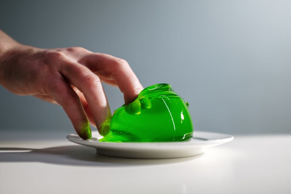 Close-up of a hand pressing a vibrant green gelatin dessert on a white plate.