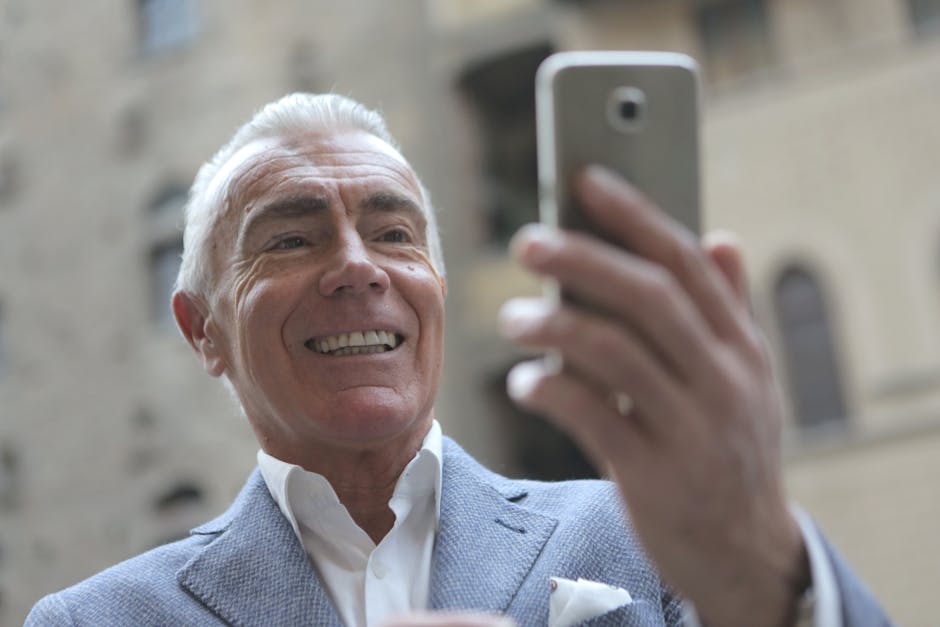 Elderly man in a suit smiling while taking a selfie outside.