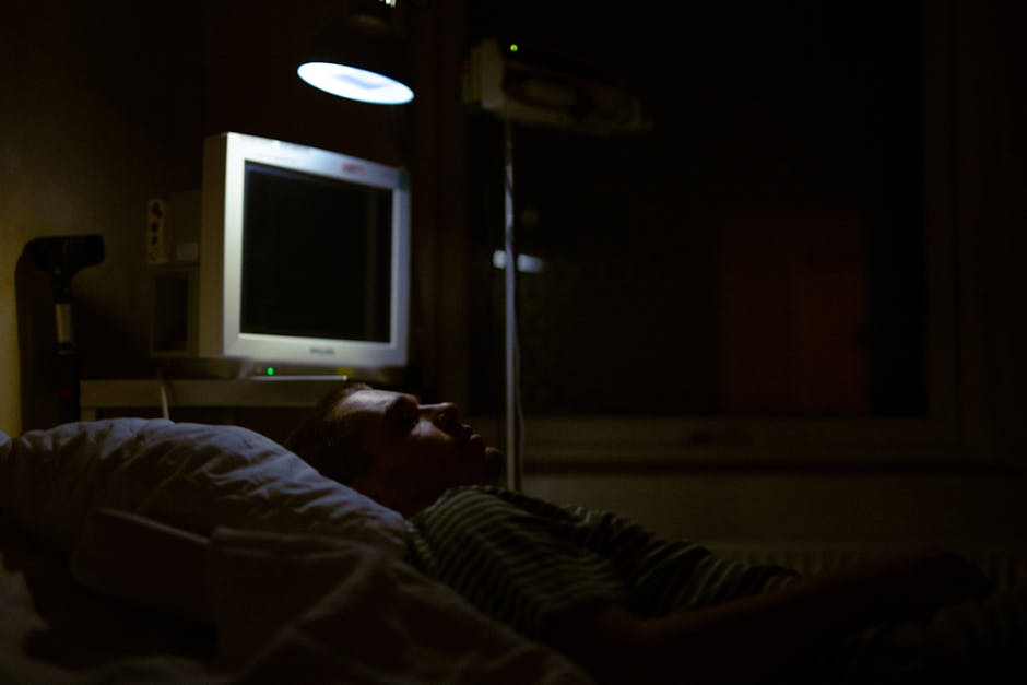 Man lying on a hospital bed under dim light, with medical equipment visible.