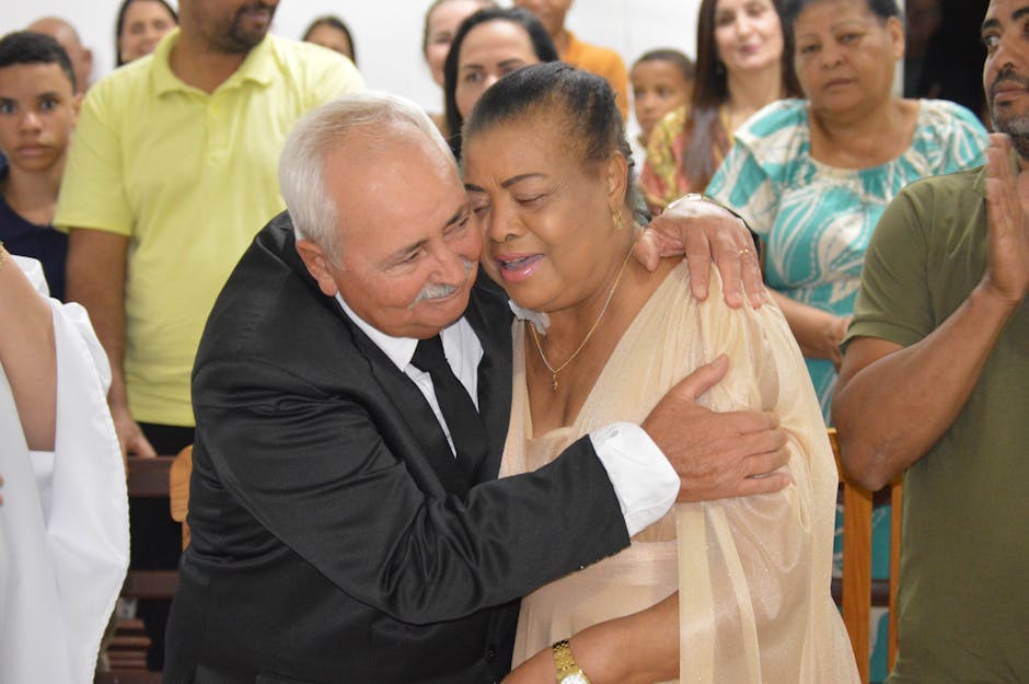 Senior couple hugging warmly at a social gathering surrounded by friends and family.