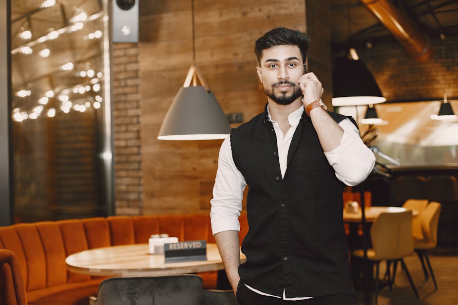 Confident young man in a vest using a phone inside a modern restaurant setting.