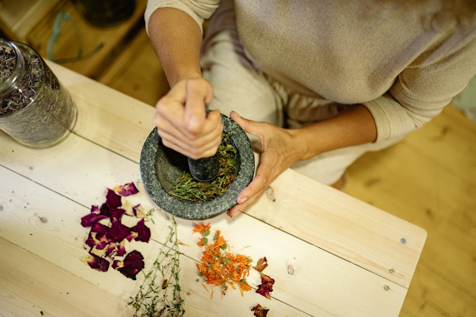 Close-up of hands grinding herbs and flowers in a mortar on a wooden table.