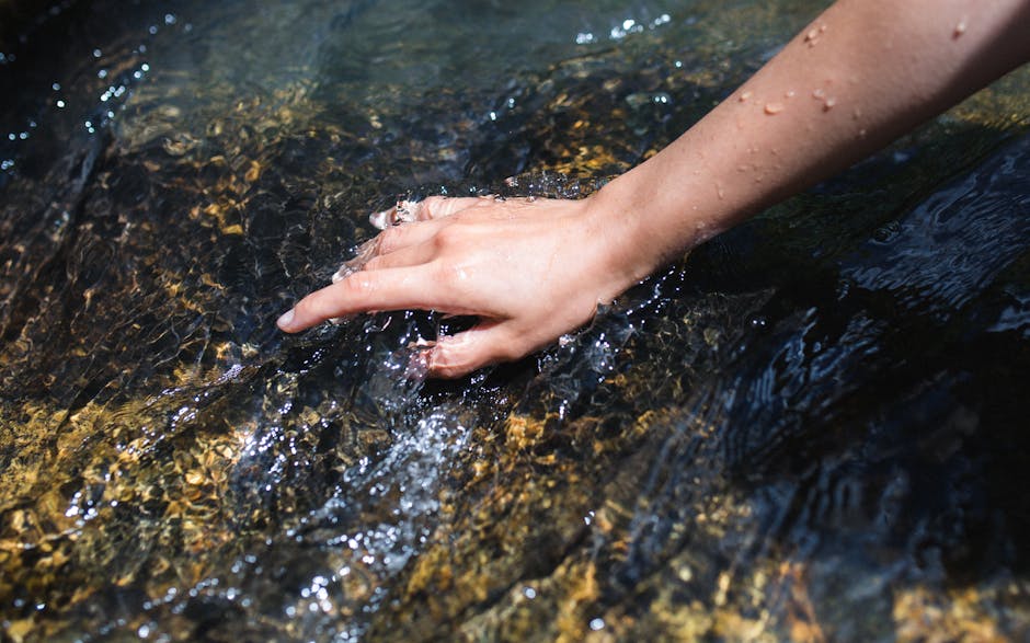 A close-up of a hand touching the clear water of a flowing stream, evoking freshness.